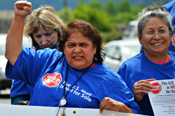 Woman in a blue shirt with a postal service slogan raising fist and holding a sign