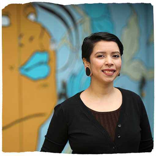 Jude Perez smiles in front of an abstract mural of a person with blue lips in Southeast Portland.