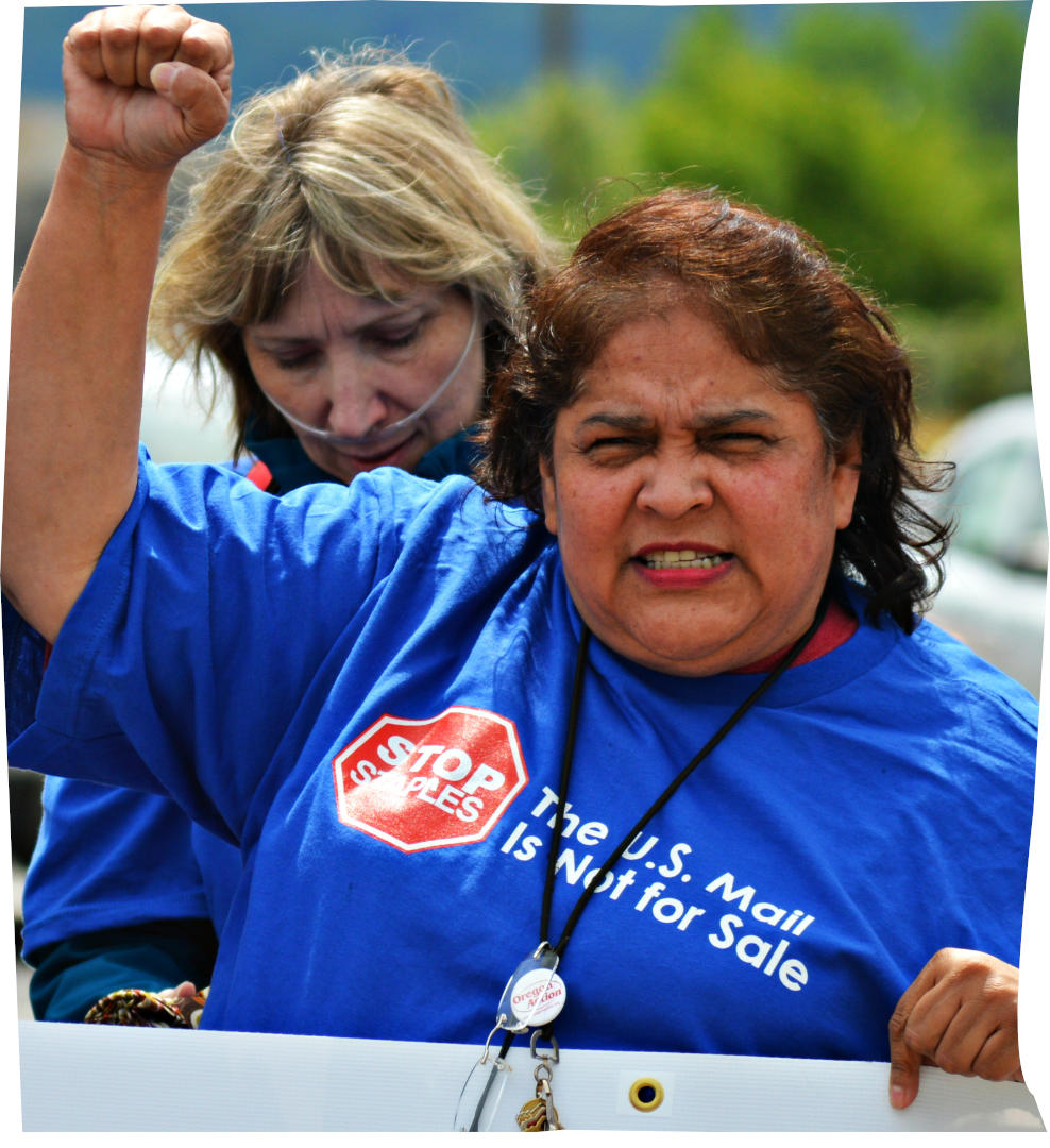Woman in a blue shirt with a postal service slogan raising fist and holding a sign