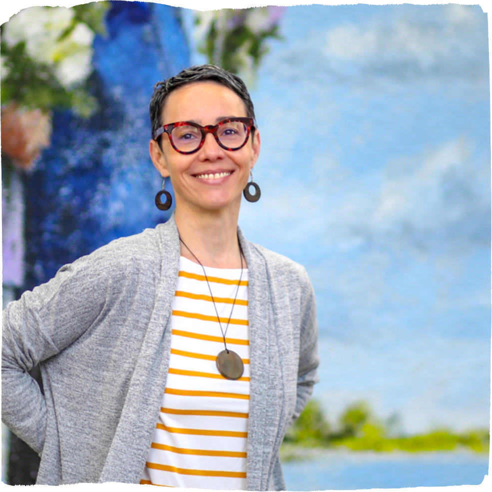 Violeta Rubiani, Director of Programs, wearing a striped shirt and grey cardigan standing in front of a light blue background.