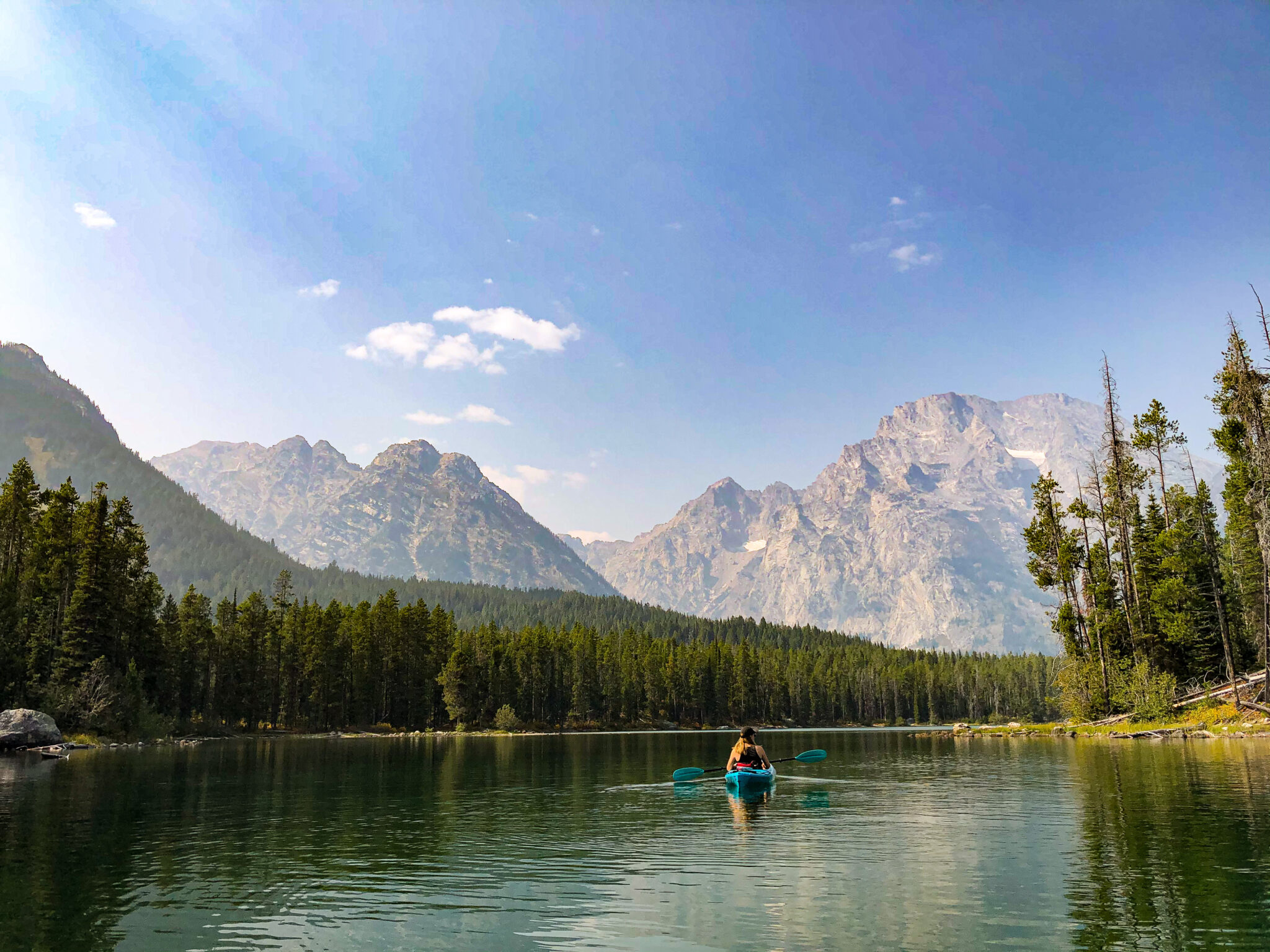 A kayaker floats serenely on an alpine lake with mountains rising in the distance.