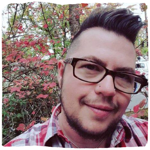 Oblio Stroyman, wearing glasses and a plaid shirt, smiles in front of a tree in full spring bloom.