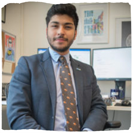 Ricardo Lujan-Valerio poses in a blue suit in front of his computer.