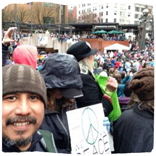 Ubaldo Hernandez stands amongst a crowd of protestors wearing a green and beige beanie.