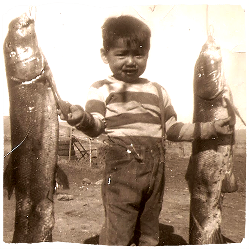 A child poses between two fish in an old, sepia-toned photo.