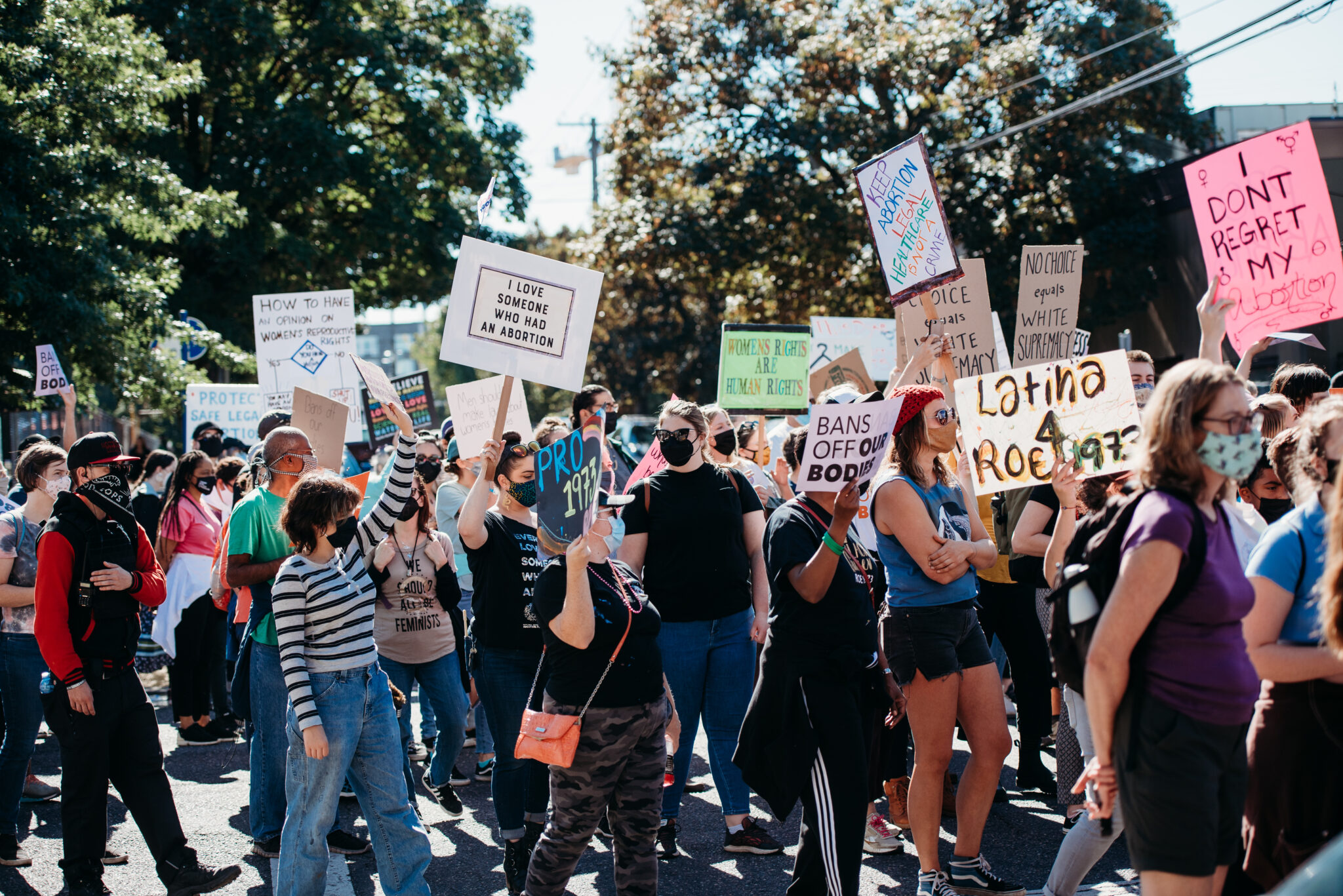 A group of protestors march through the street carrying signs supporting access to reproductive health services.