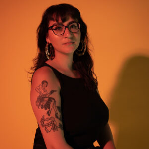 Emilly Prado poses for an orange-tinted photo wearing all black.