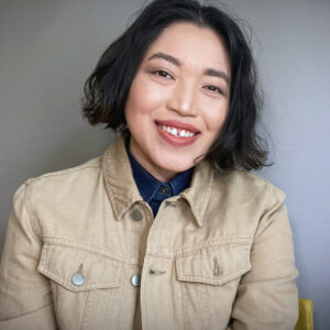 Artist May Maylisa Cat smiles wearing a khaki-colored jacket. 