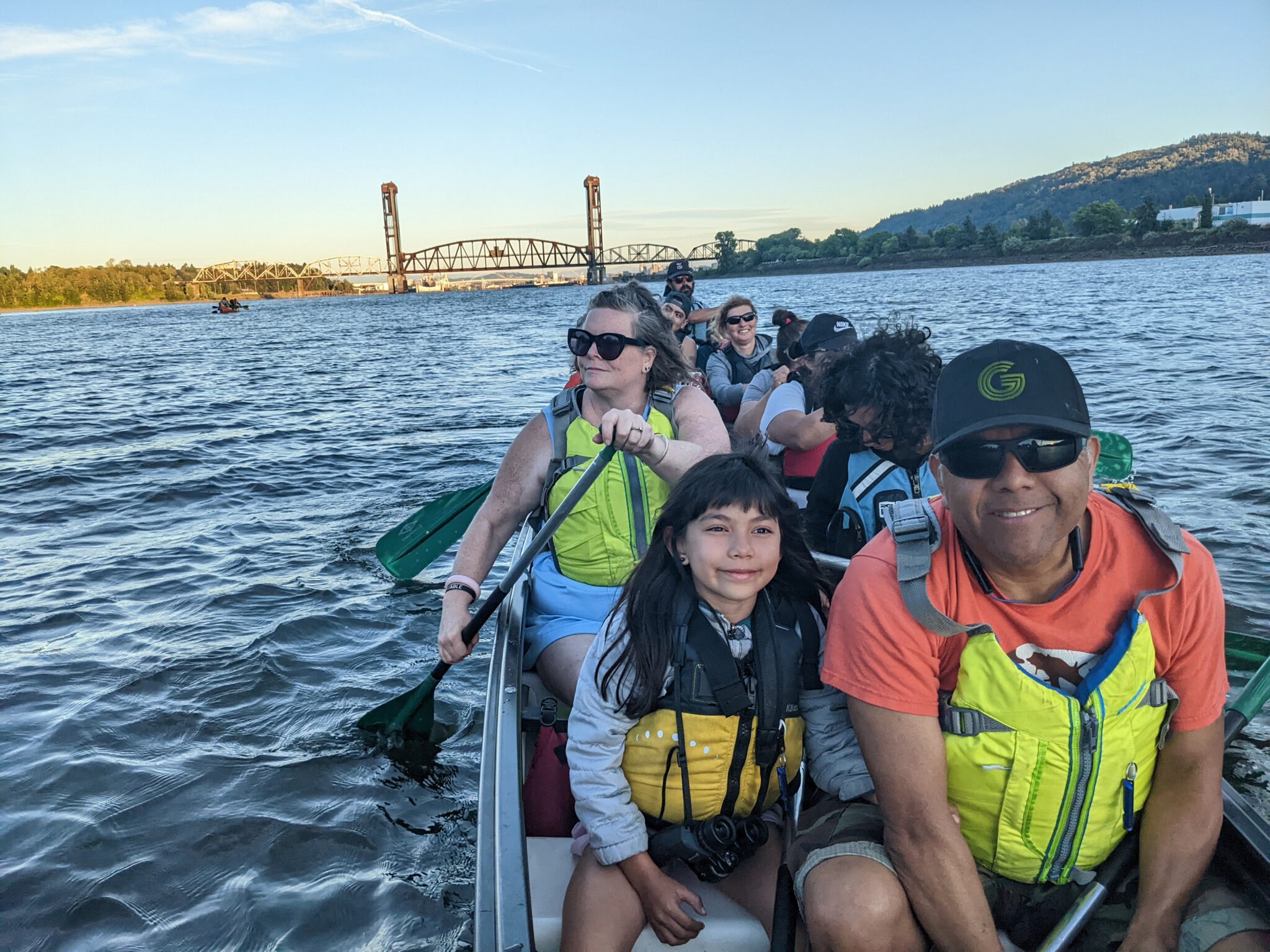 A group of kayakers wearing PFDs paddle the Willamette River on a sunny day.