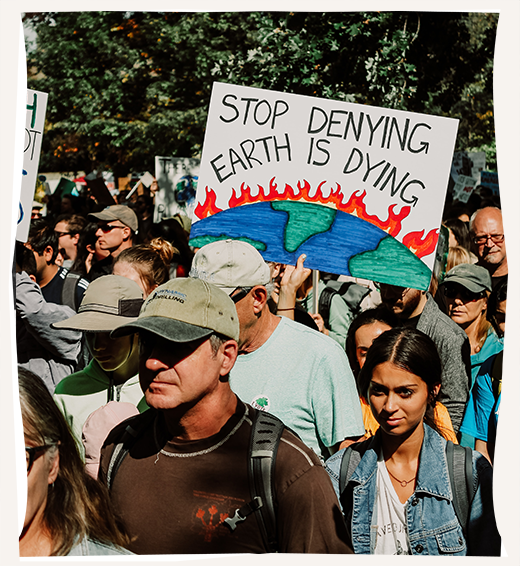 Protestors march in a climate rally. One is holding a sign with the image of the earth on fire that reads, "stop denying earth is dying."